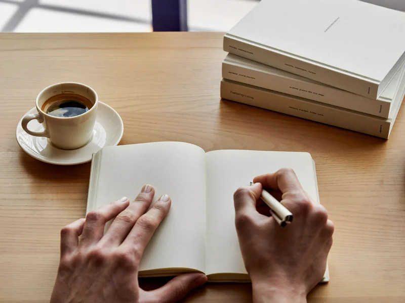 Illustration: Hände schreiben in ein Notizbuch neben Kaffee und Lehrbüchern
